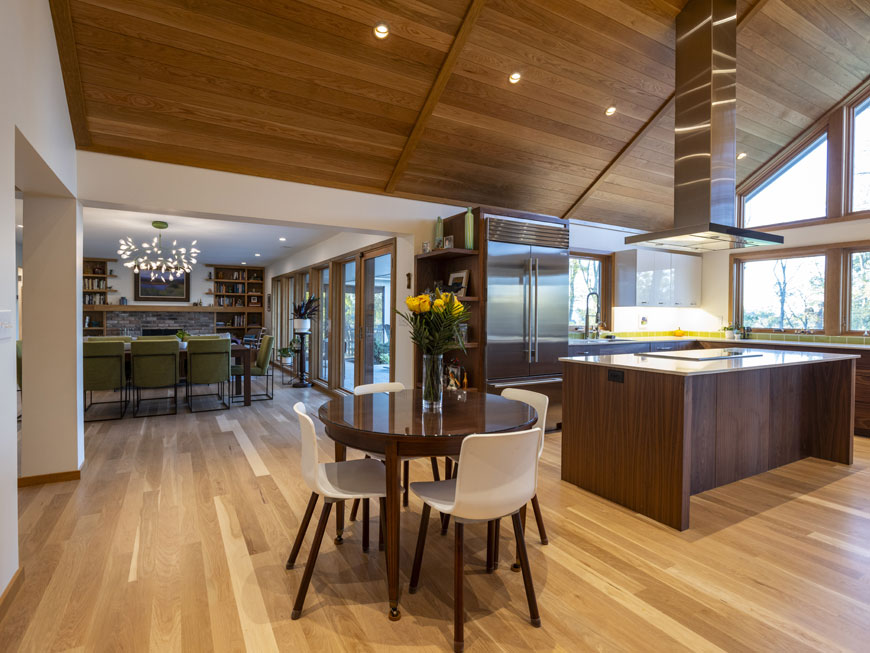 Modern kitchen redesign features a small kitchen table, cooktop island with stainless steel appliances. Beyond, the living space can be seen with mid-century atomic design elements.