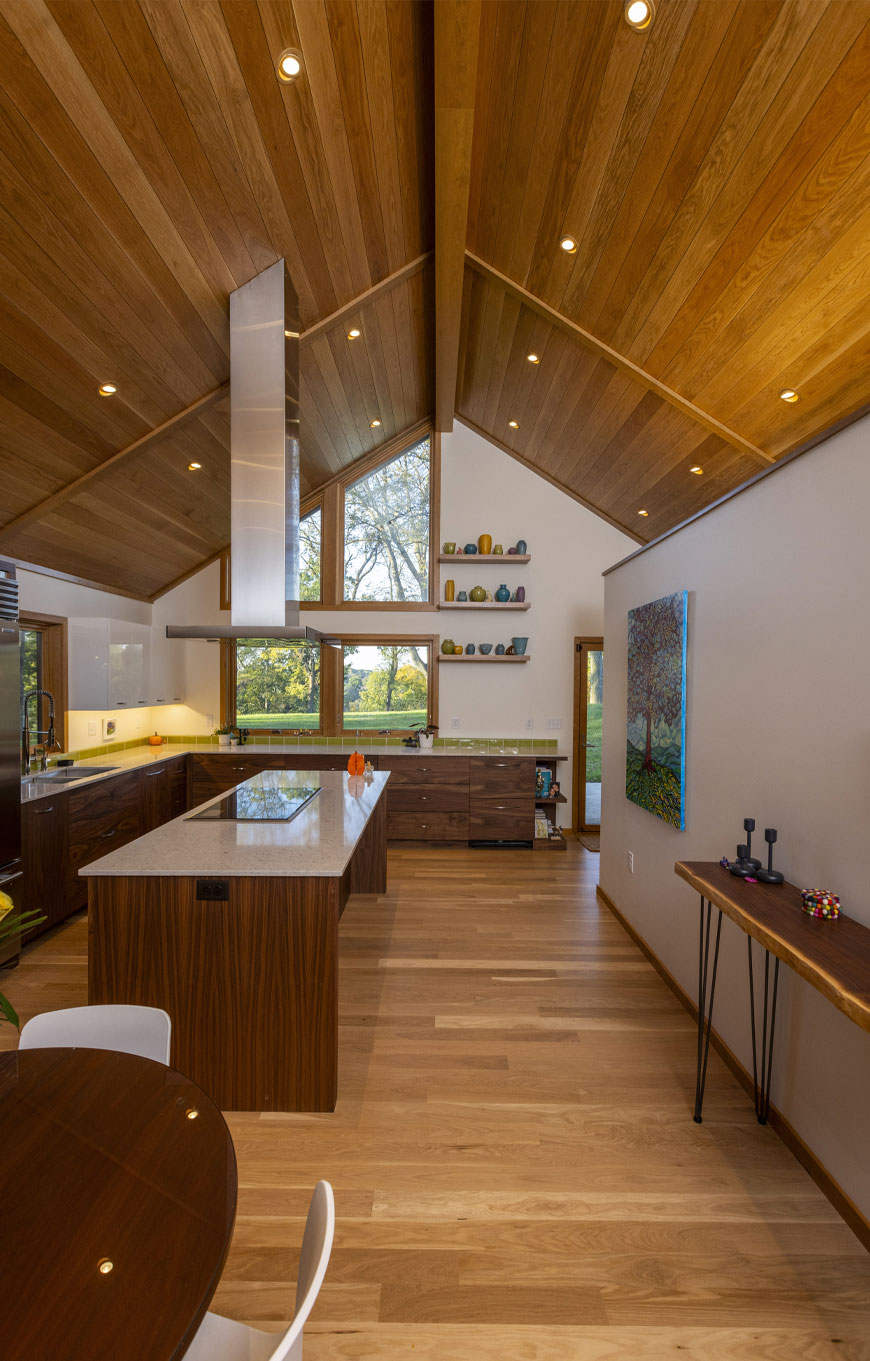 Kitchen of mid-century modern home remodel in Kentucky. Kitchen features lofted ceilings with wooden cladding, a cooktop island, and views to the backyard.
