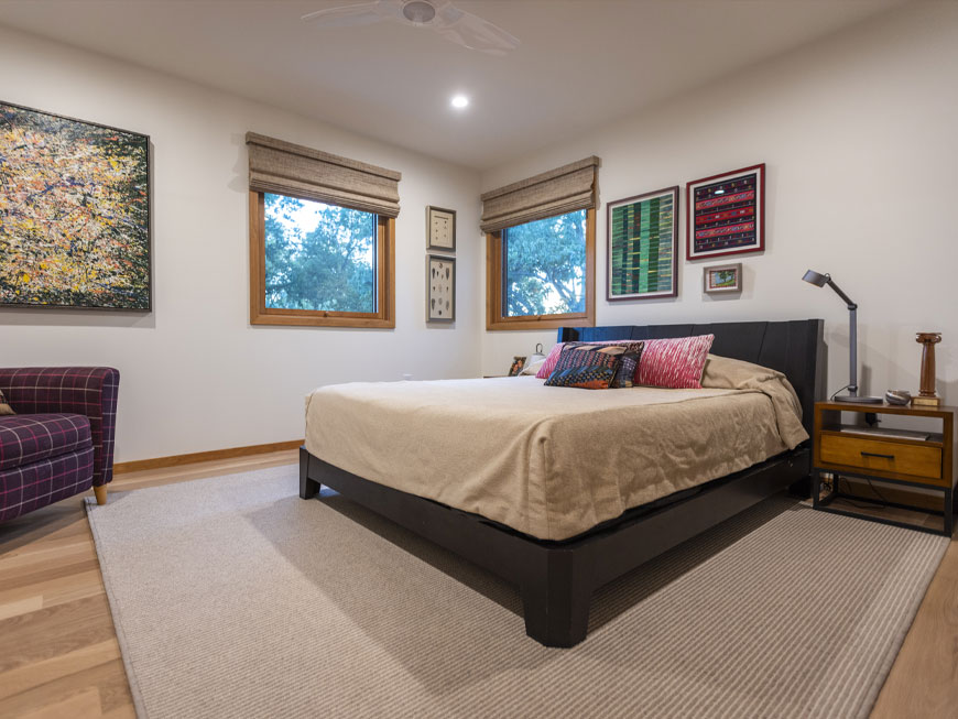 Simple bedroom design features artwork adorning white walls, a plaid chair, a modern bed frame.