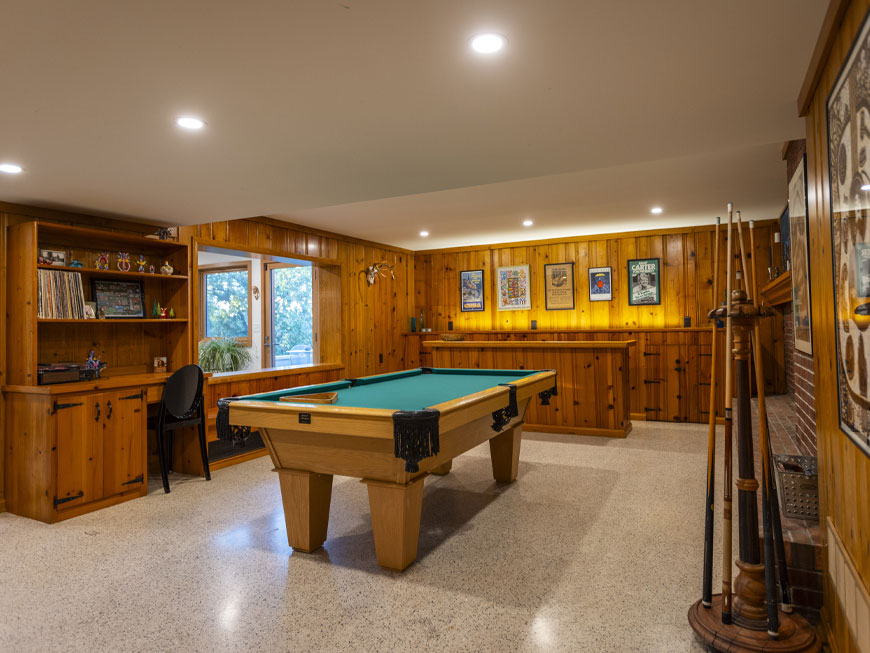 Restored pine paneled lower level rec room featuring a central pool table, original bar and open window to newly added art studio.