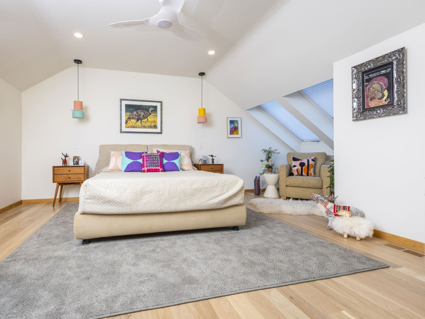 Simple bedroom features bright white walls, colorful hanging lamps, and modern, colorful pillows. Art adorns walls and embraces playful nature of room.