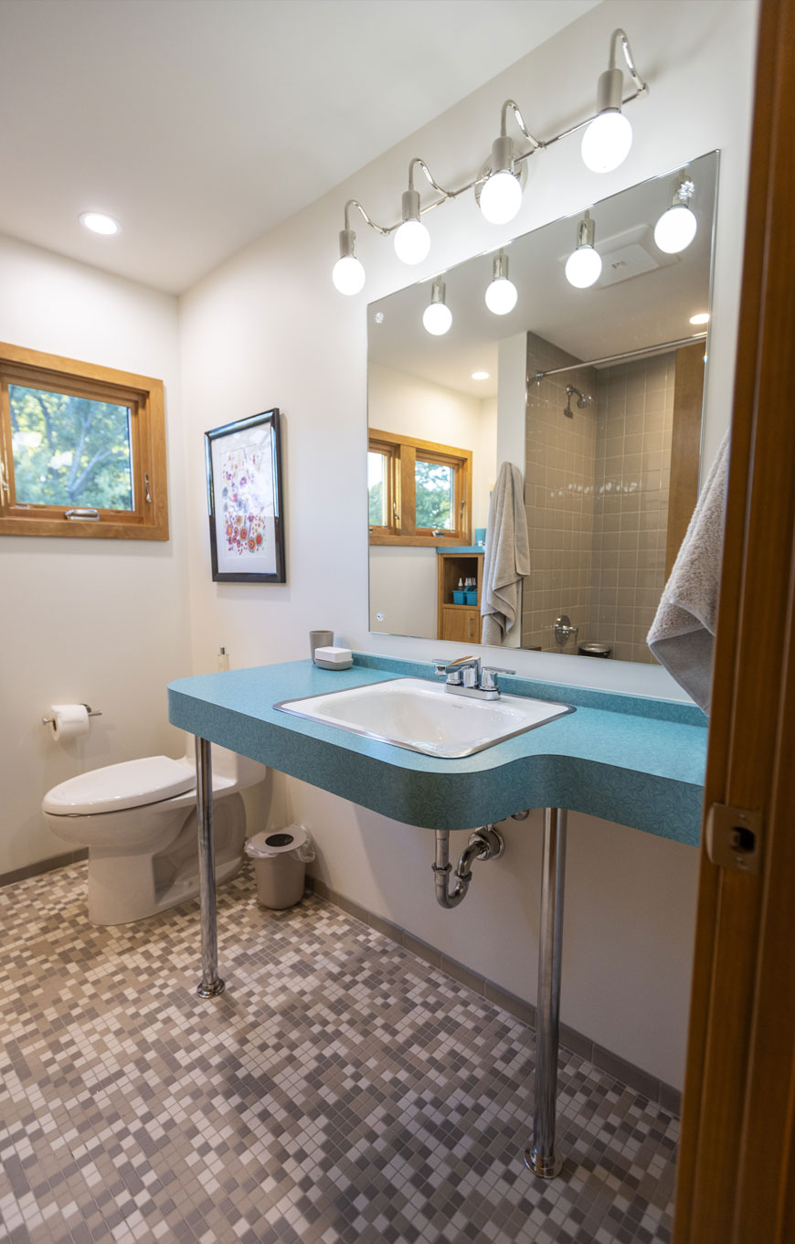 Bathroom remodeled with mid-century atomic aesthetic features teal sink, metal fixtures, and grey, pixelated floor tiles. Part of home remodel by Chris Kepes.