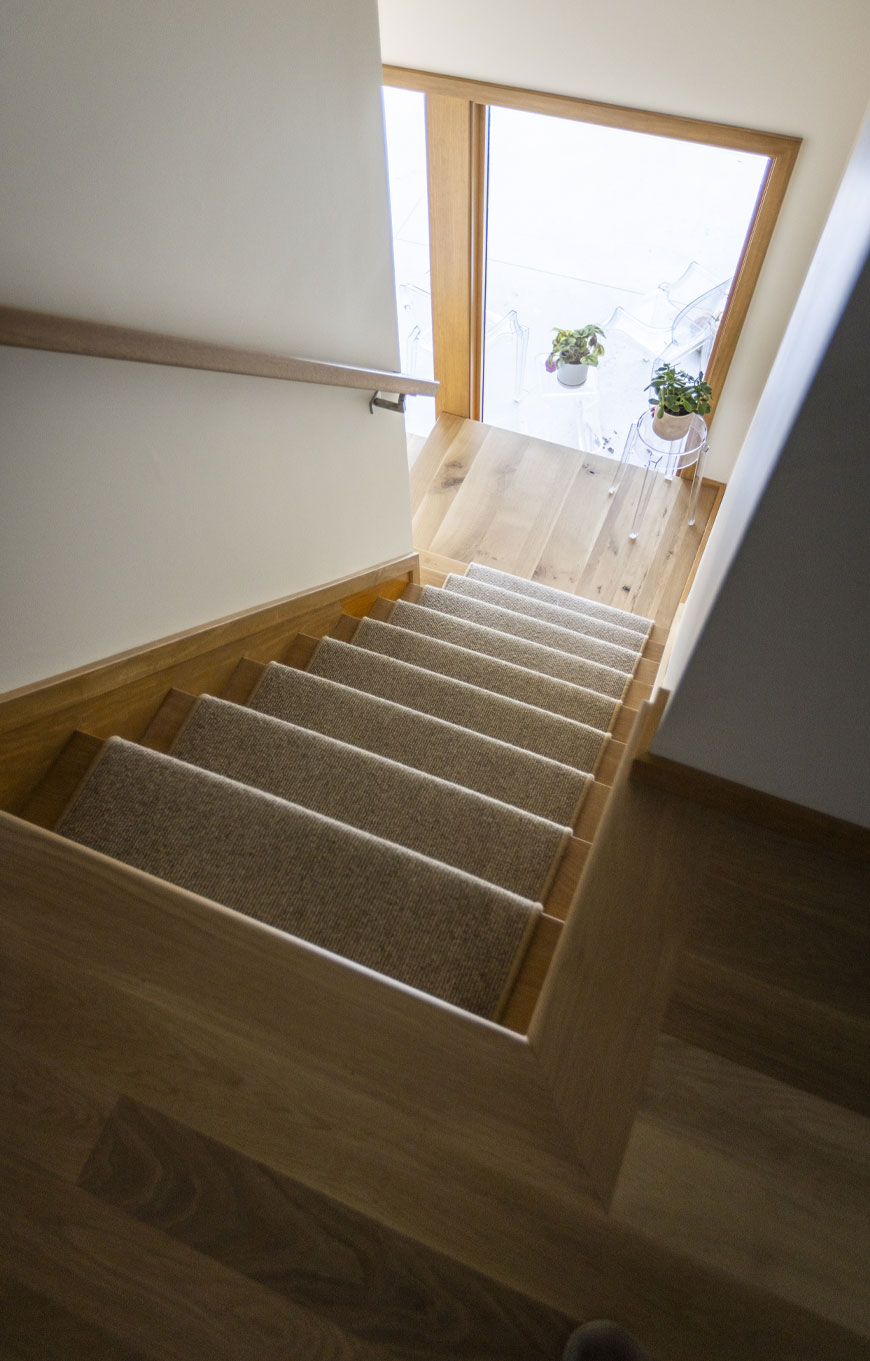 Stairs to first level feature subtle runner and windows to patio.