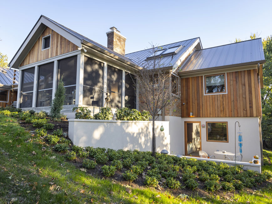 Back view of home shows off the covered porch addition and updated landscaping. Updated wood cladding alternates with brick on facade of house. Remodel by Chris Kepes and Kepes Architecture.