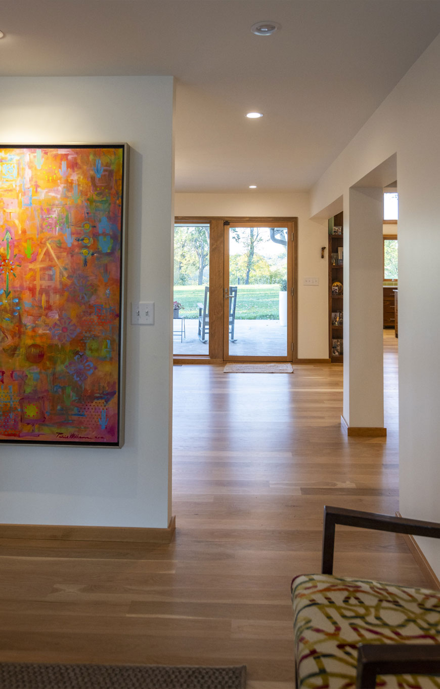 Entry way to home remodel in Kentucky. Interior design is modern with white walls and colorful art on display. Wooden floors.