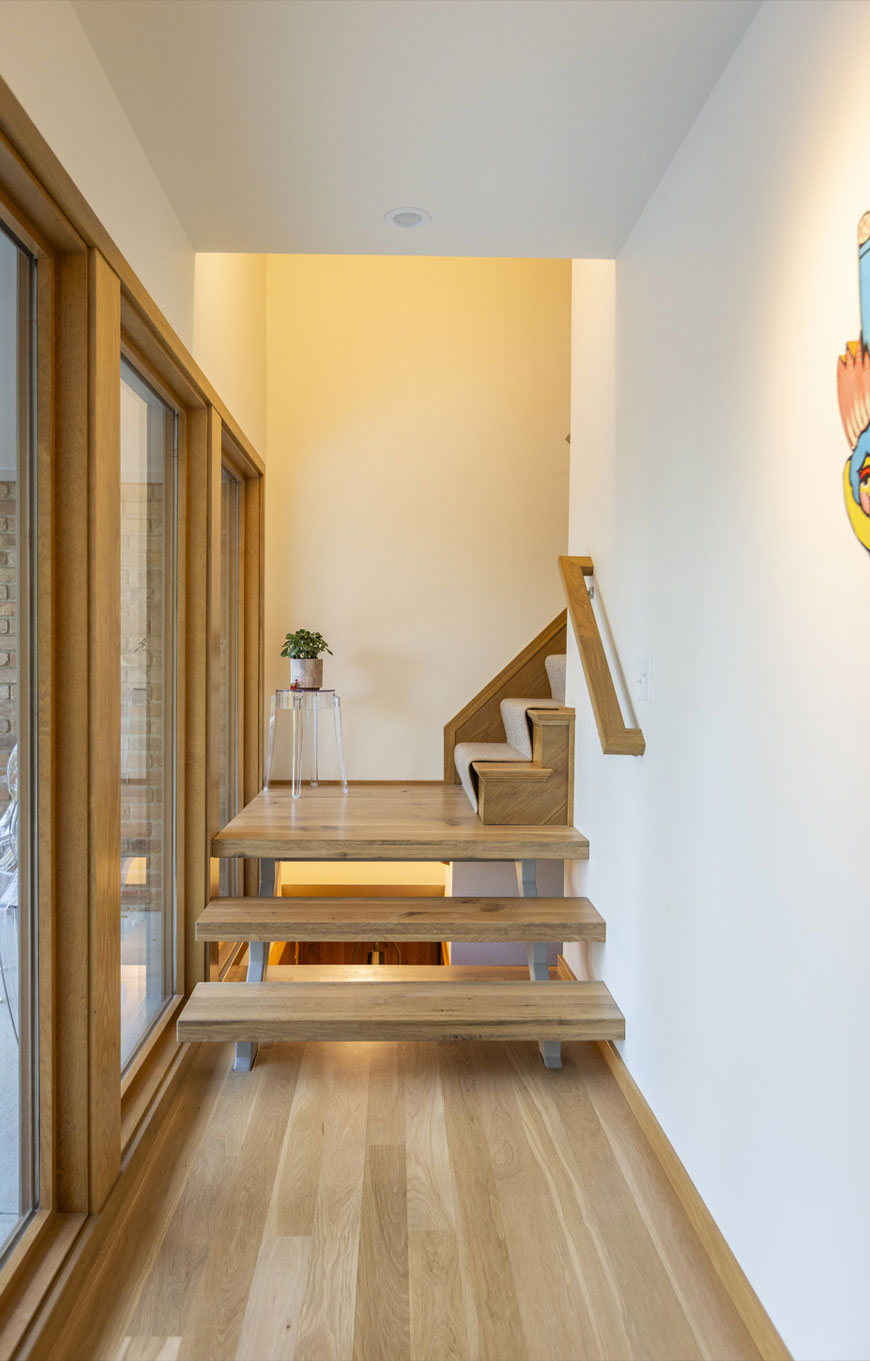 Simple, modern steps lead to second floor in mid-century modern home remodel by Chris Kepes. Steps are made from blonde wood, walls are white and simple.
