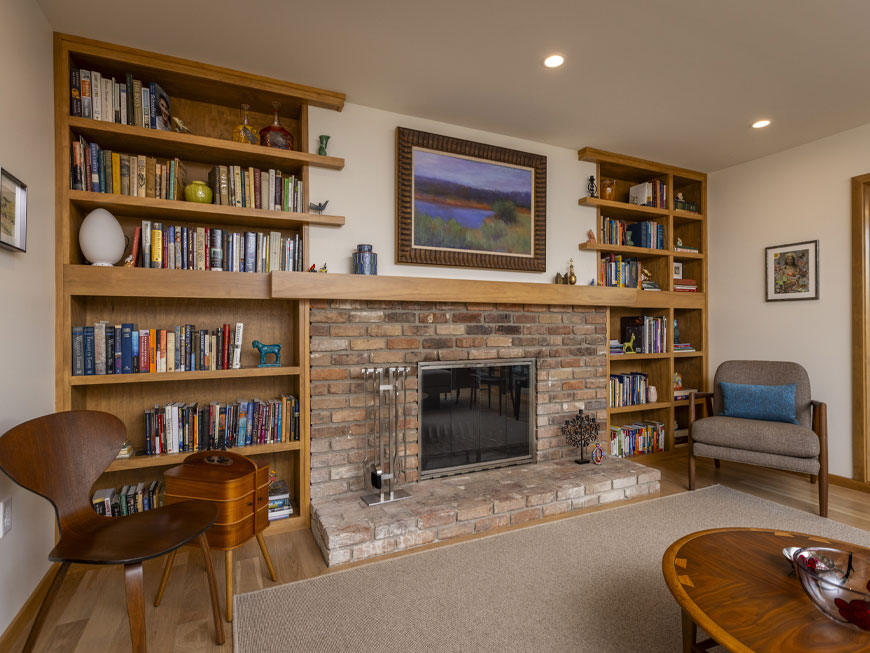 Two new pine bookcases flank on original brick fireplace in living space. Furniture and decor reflect mid-century atomic design elements.
